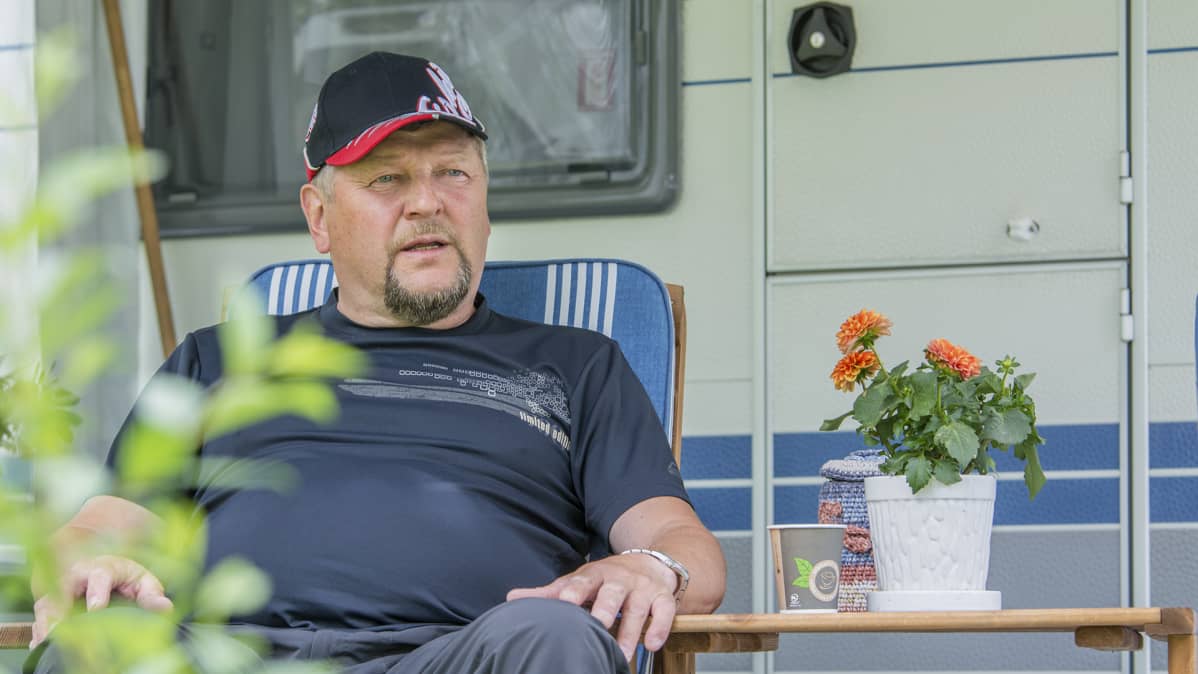 Mies istuu asuntovaunun edustalla tuolissa.