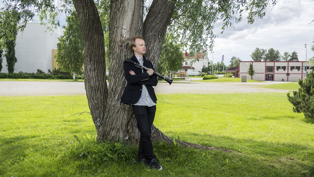 Lauri Sallinen nojaa puuhun Kuhmotalon vieressä.