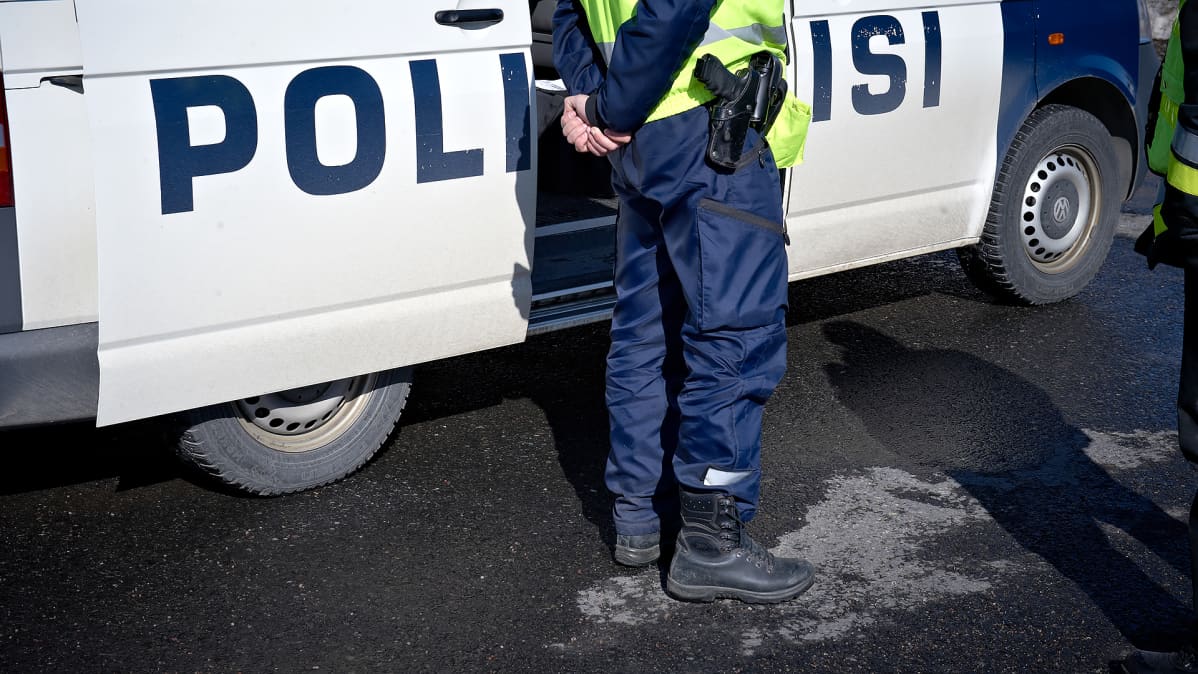 Poliisi seisoo poliisiauton edessä.