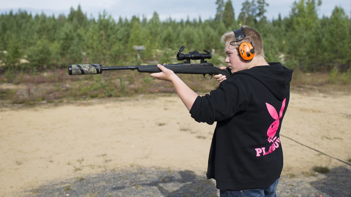 Nuori mies kuulosuojaimet päässä tähtää kiväärillä, jossa on äänenvaimennin