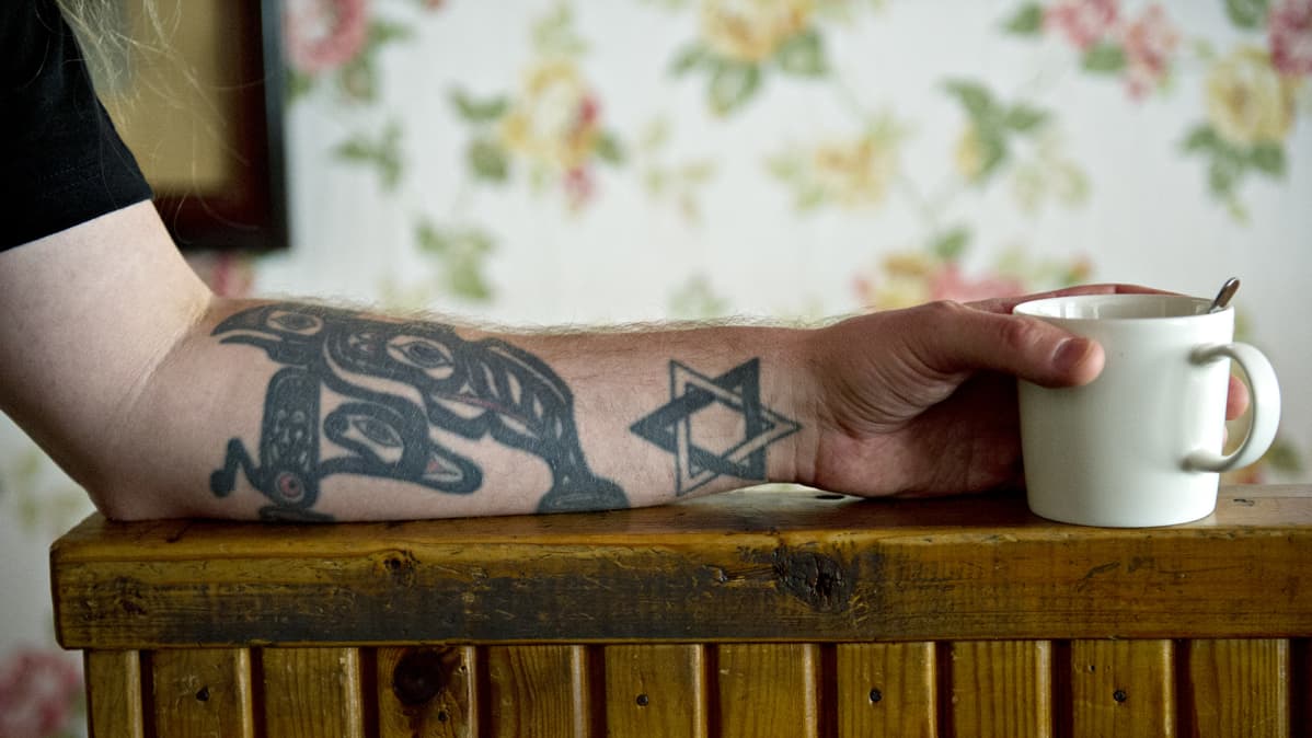 Tatuoitu käsi pitelee kahvikuppia portaiden kaiteella.