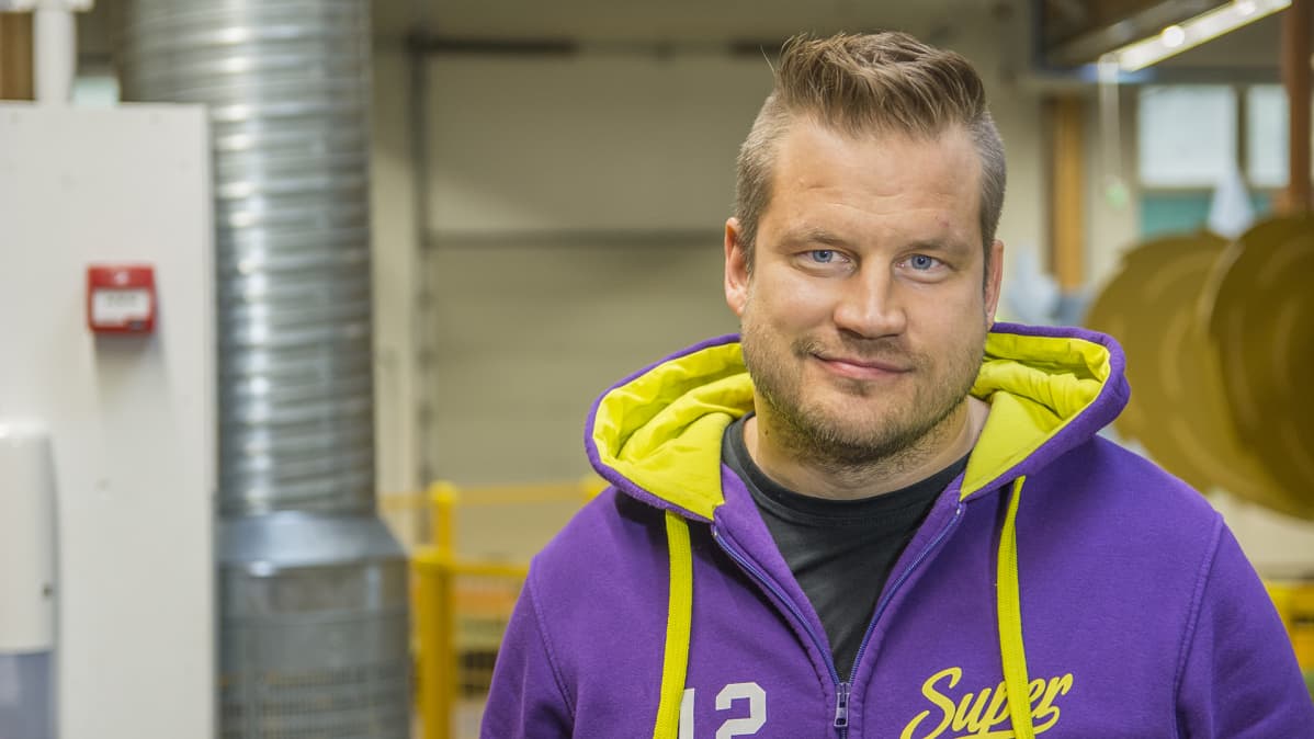Pikkupartainen mies katsoo kameraan, päällä violettihuppari jossa keltainen huppu.