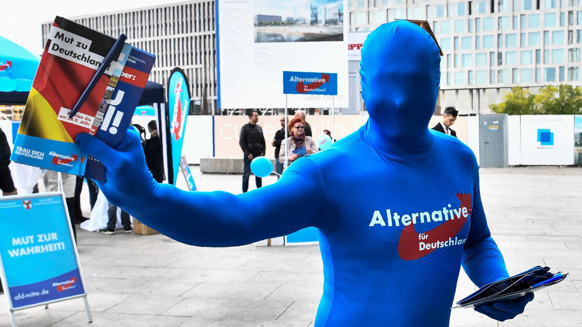 Siniseen haalariin pukeutunut aktivisti jakaa AfD-puolueen mainoksia.