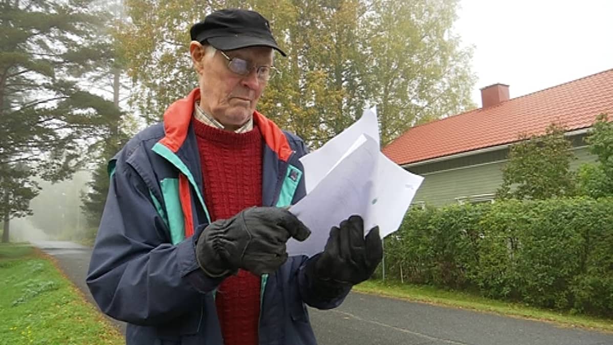 Silmälasipäinen vanhempi mies tutkiin papereitaan ulkona