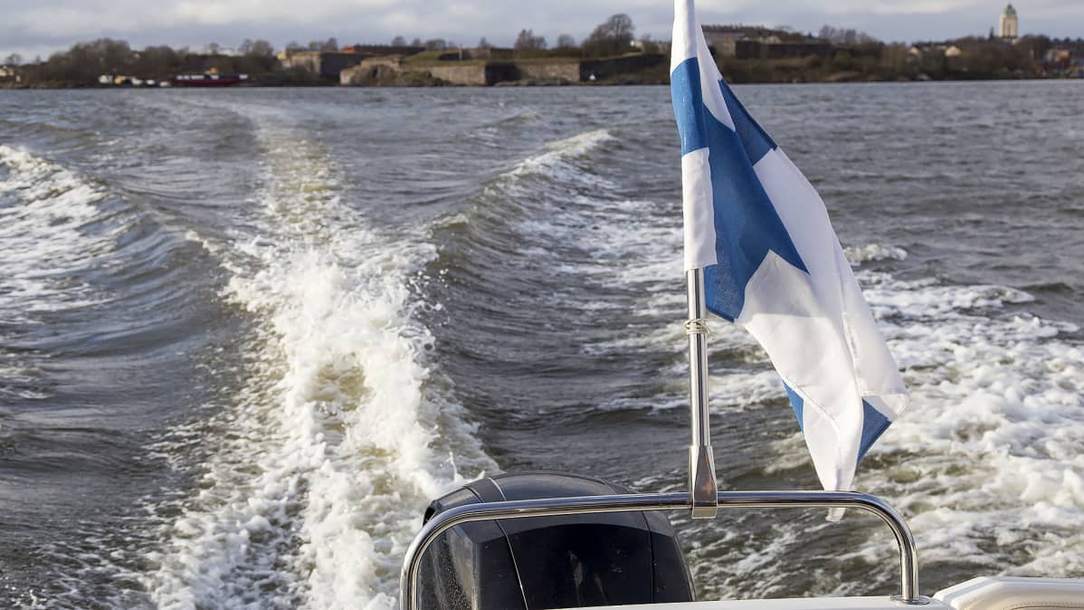 Veneen Suomen lippu liehuu tuulessa ja Suomenlinna näkyy taaempana.