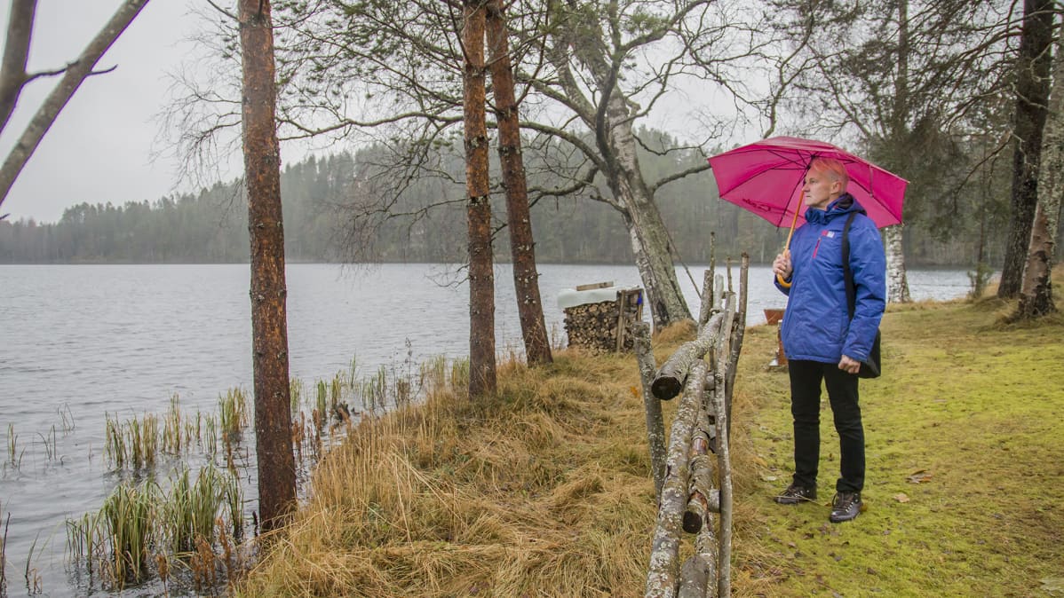 Mies katsoo sateessa järvelle rannalta.