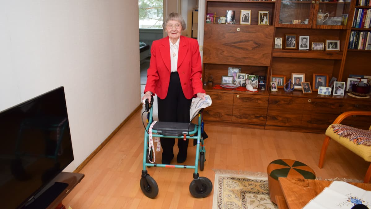 Auli Peltonen kävelee olohuoneeseen rollaattorin kanssa.
