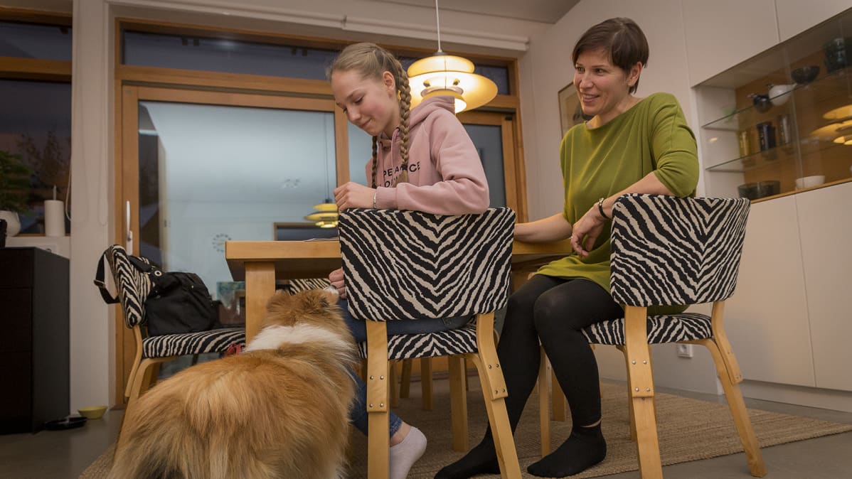 Äiti ja tytär sekä koira keittiön pöydän ääressä.