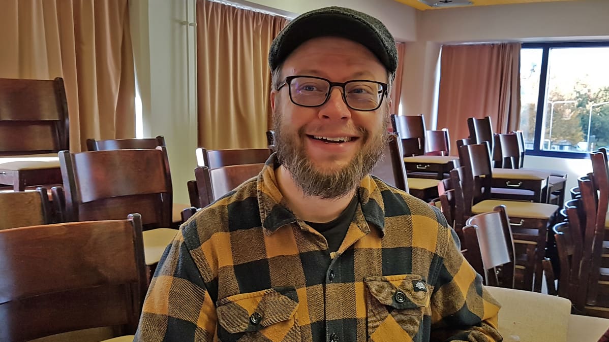 Sami Taponen seisoo huoneessa ja hymyilee