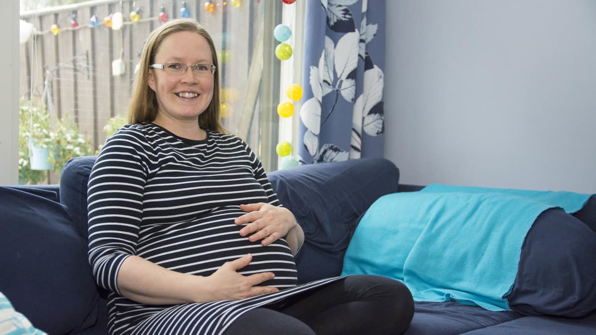 Viidettä lastaan odottava Anne Heikkinen istuu kotisohvallaan.