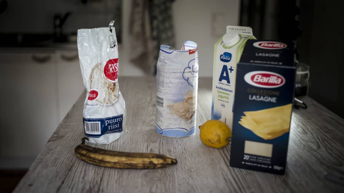 Banaani ja sitruuna, lasagnelevypaketti, puuroriisipussi ja piimäpurkki pöydällä.