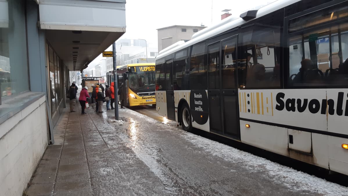 Kaksi linja-autoa pysäkillä. Matkustajia nousee kyytiin.