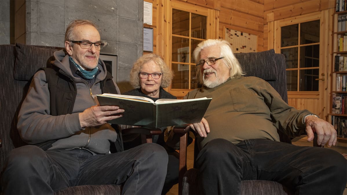 Reino Kuivalainen, Sirpa Sulopuisto ja Heikki Turunen lukevat leikekirjaa taiteilijatalo Hupelissa.