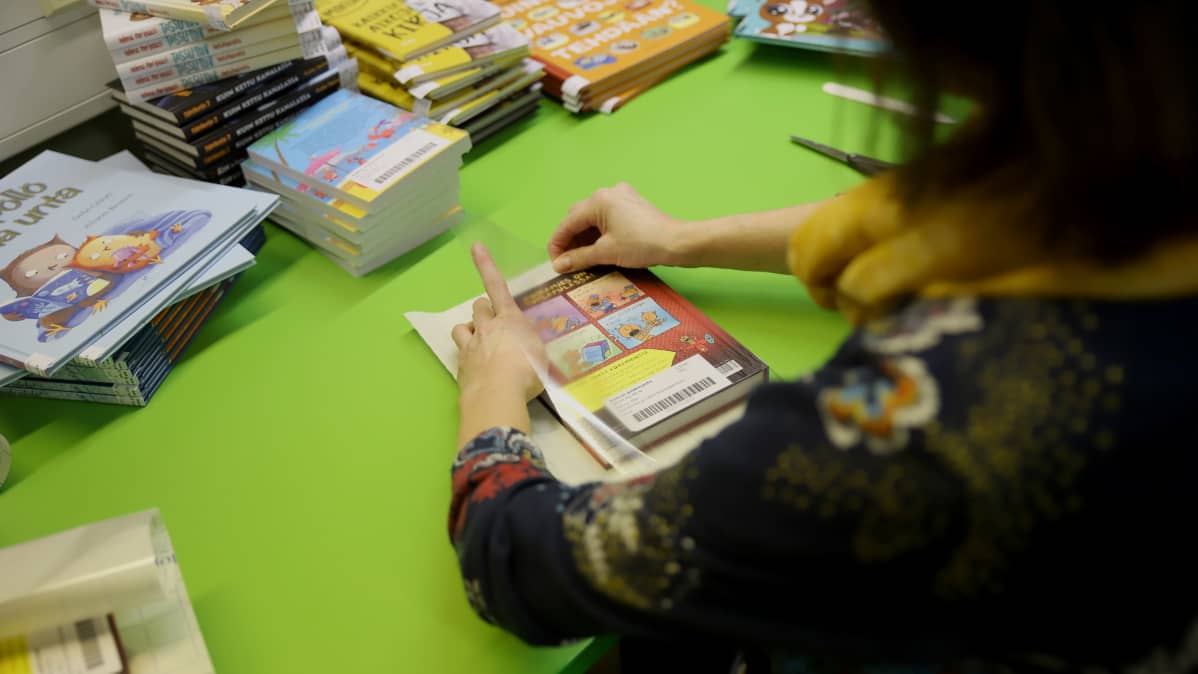 nainen päällystää kirjoja kontaktimuovilla