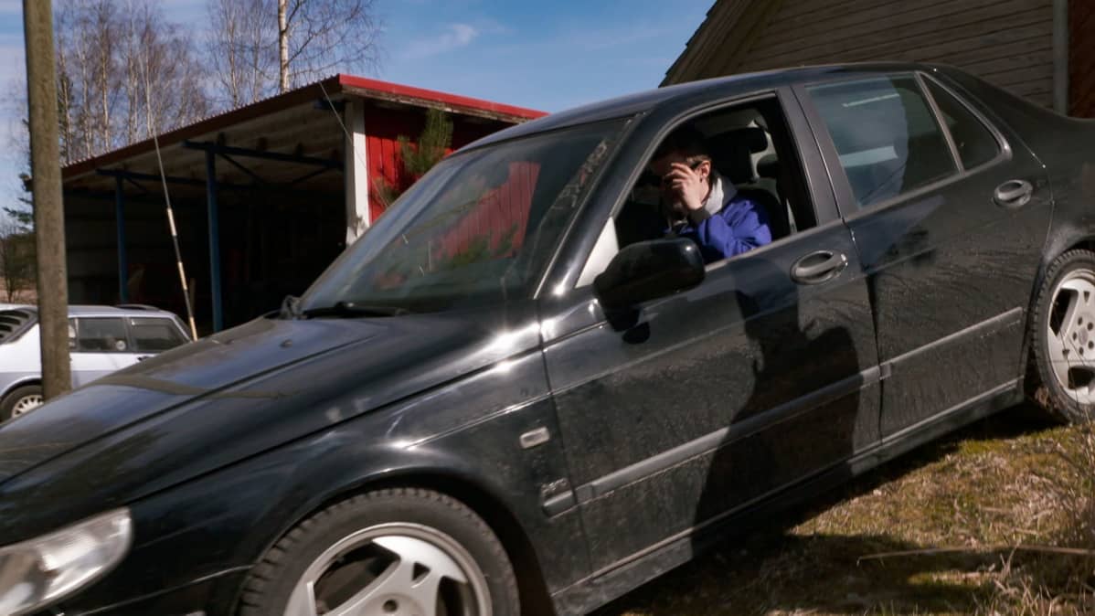Arttu Väisänen istuu Saab 9-5- Aerossa, laittaa aurinkolaseja päähän.