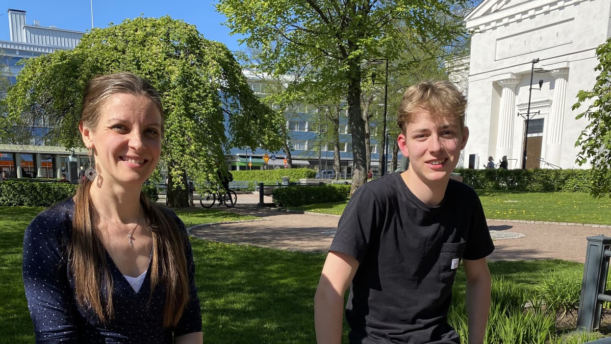 Kuoronjohtaja ja nuorisokuorolainen istuvat puistossa aidalla toukokuussa