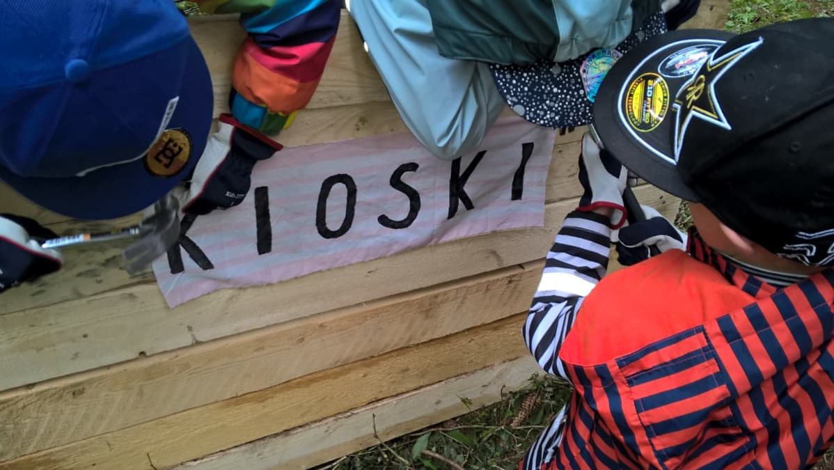 Lasten majaleirillä rakennettin kioski, joka tarvitsee kyltin seinälleen.