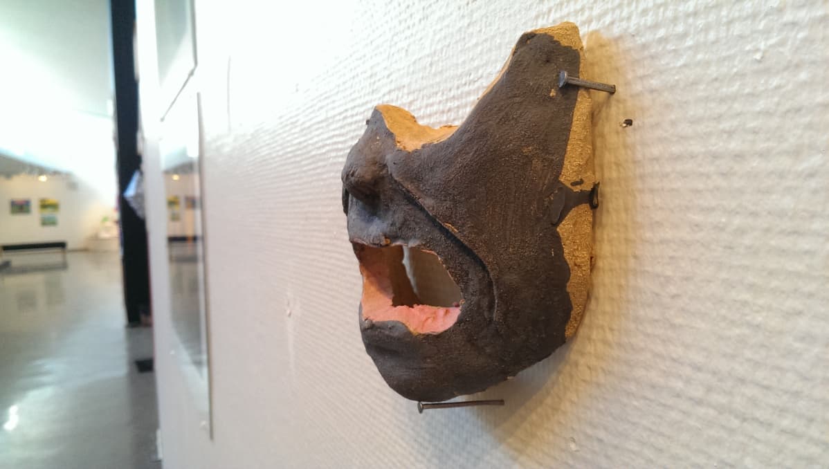 Naamio museon seinällä, puolet kasvoista puuttuu.