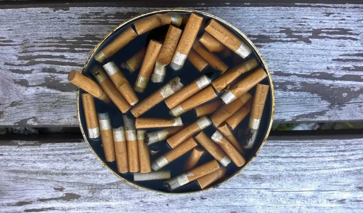 Veden täyttämä, tupakannatsoja täynnä oleva tuhkakuppi kuluneella puupöydällä.