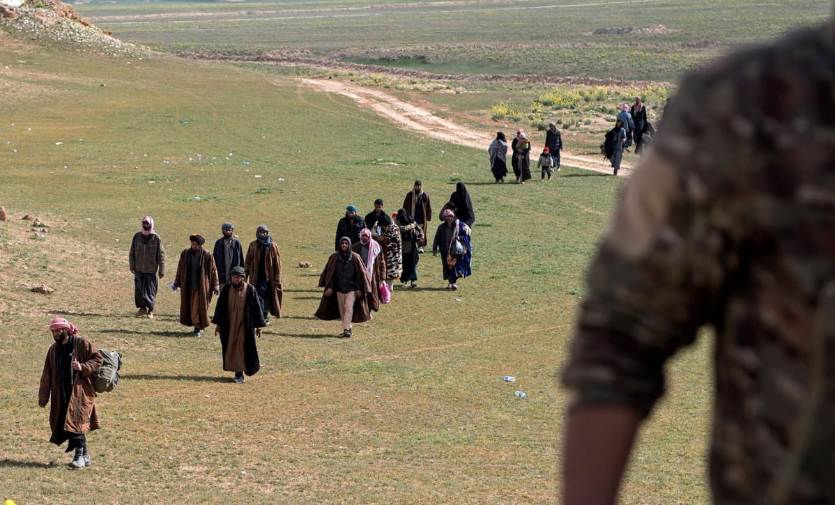 Isis-taistelijoiksi uskotut miehet ja heidän perheenjäsenensä poistuvat peltojen yli.