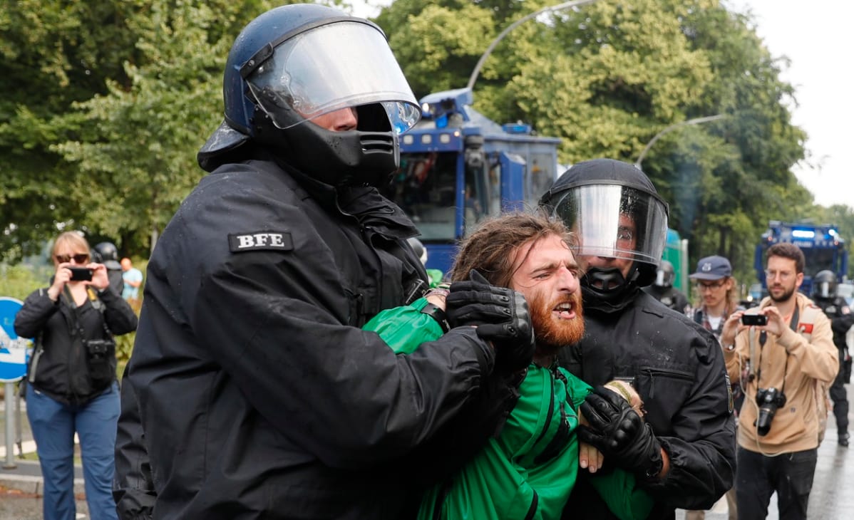 Kaksi poliisia raahaa rastatukkaista mielenosoittajaa.
