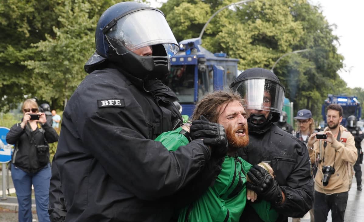 Kaksi poliisia raahaa rastatukkaista mielenosoittajaa.