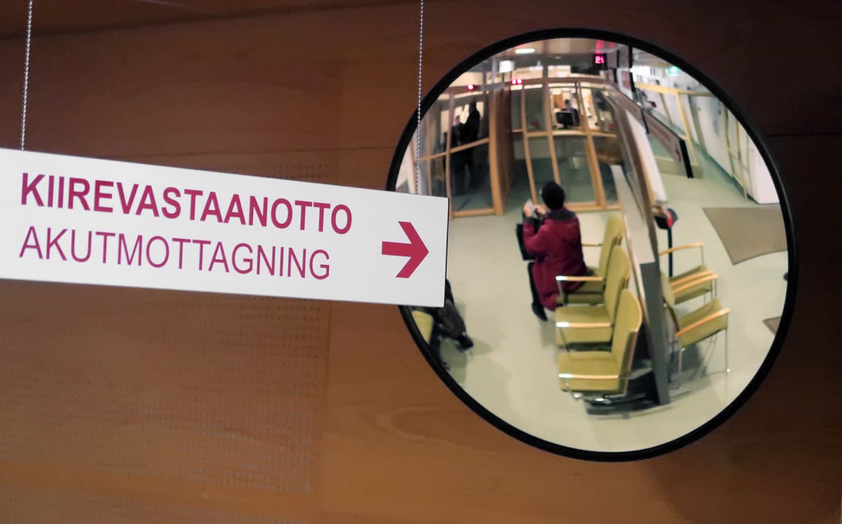 Skylt där det står akutmottagning och en spegel där en kvinna som sitter och väntar syns.