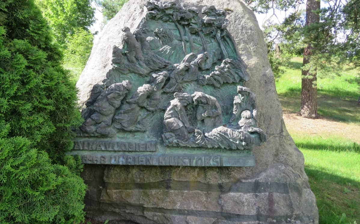 Luonnonkiveen kiinnitetty kuparireliefi nälkään nääntyvistä ihmisistä. Tekstinä "Näkävuosien 1866–1868 uhrien muistoksi".