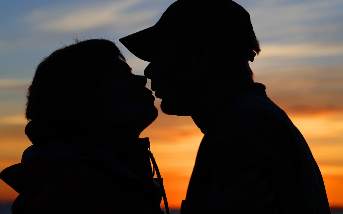 mies ja nainen suutelee auringonlaskussa