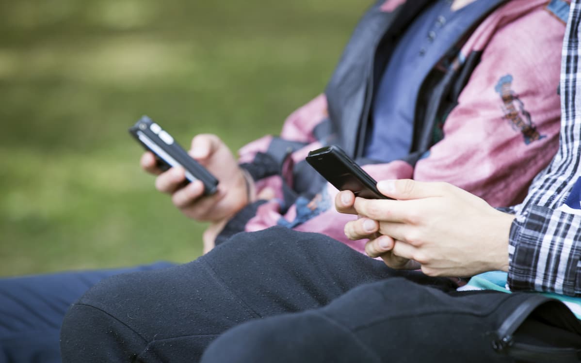 nuoria puiston penkillä kännyköiden kanssa