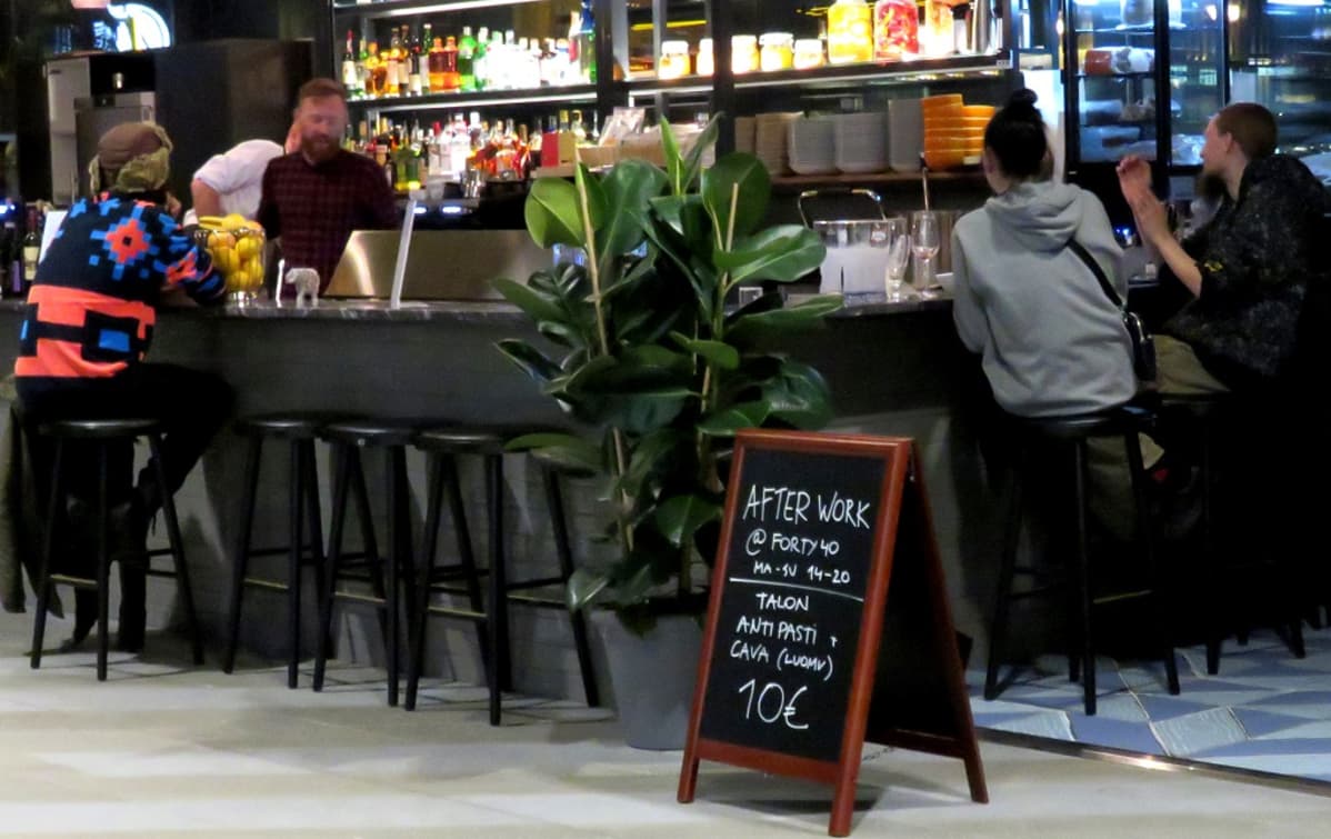 Ihmisiä baaritiskillä. Edessä liitutaulu, jossa teksti "After work, forty 40".