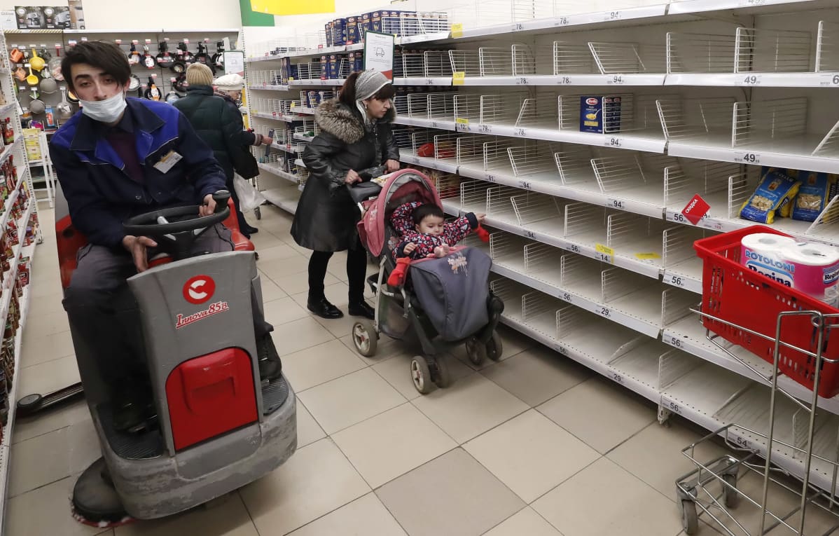 Siivooja puhdistaa lattioita ja asiakkaat kulkevat tyhjiin hamstrattujen hyllyjen ohi Auchan-ketjun marketissa keskiviikkona, Podolskissa, Moskovan ulkopuolella.