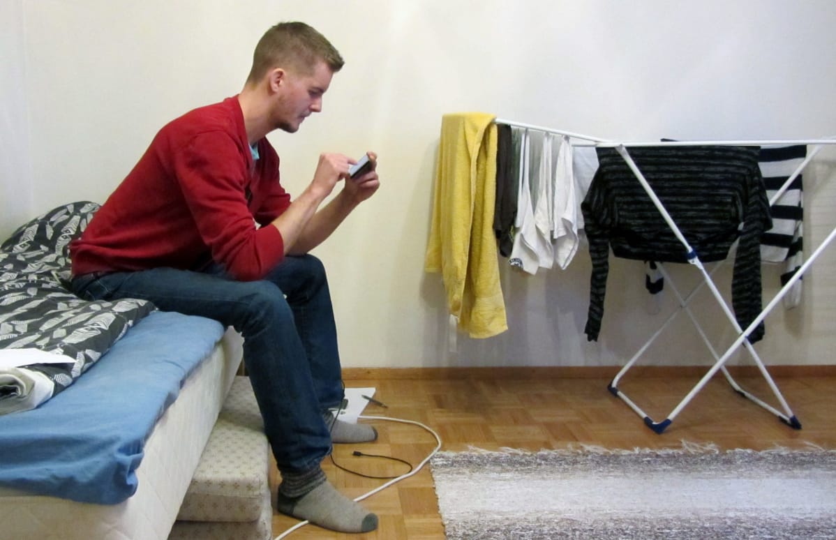 Riku Forsell istuu sängyllä ja selaa puhelinta