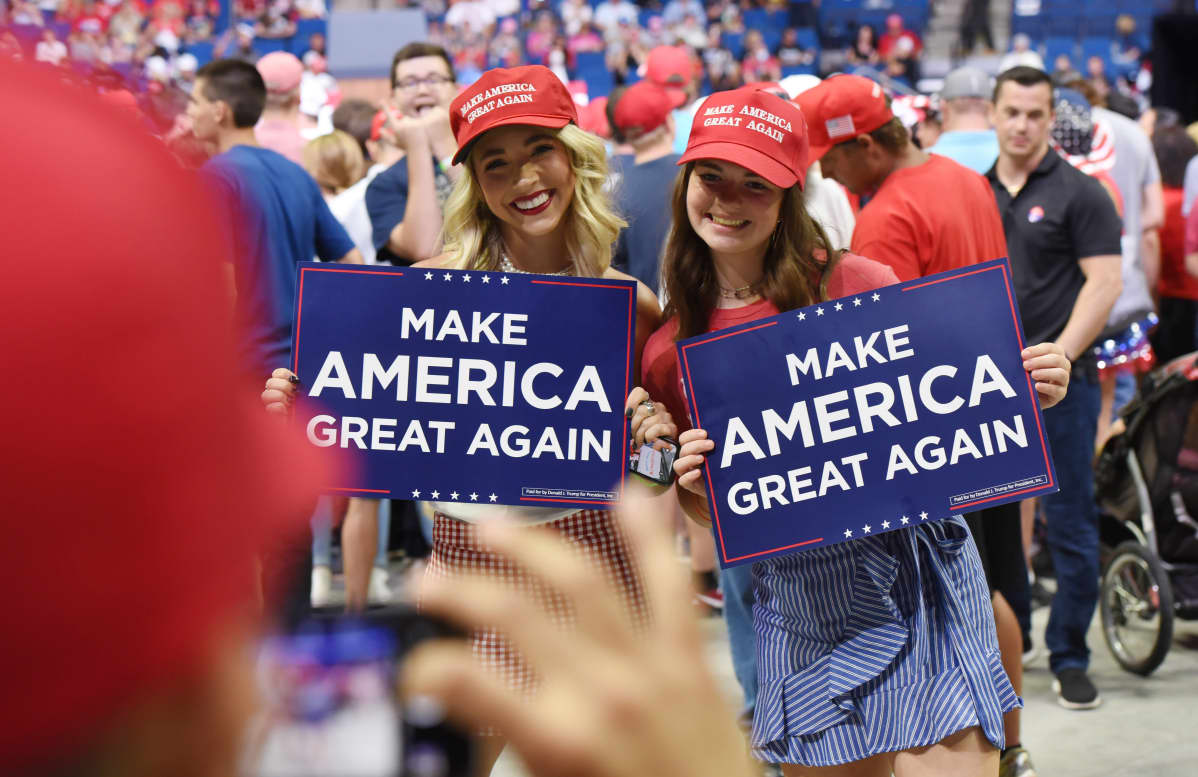 Kaksi hymyilevää tyttöä pitelee käsissään kylttejä, joissa lukee Make America great again.