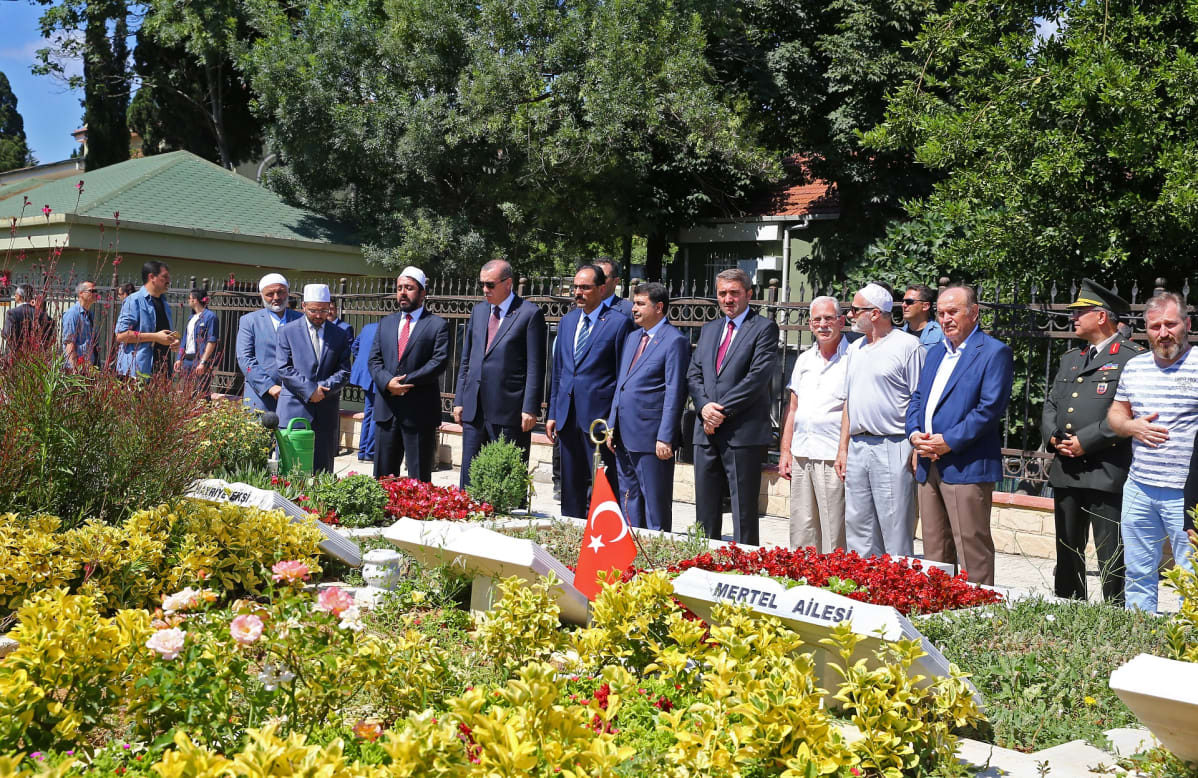 Erdoğan ja lukuisia muita miehiä seisoo hautojen edessä. Hautausmaalla on myös Turkin lippu.