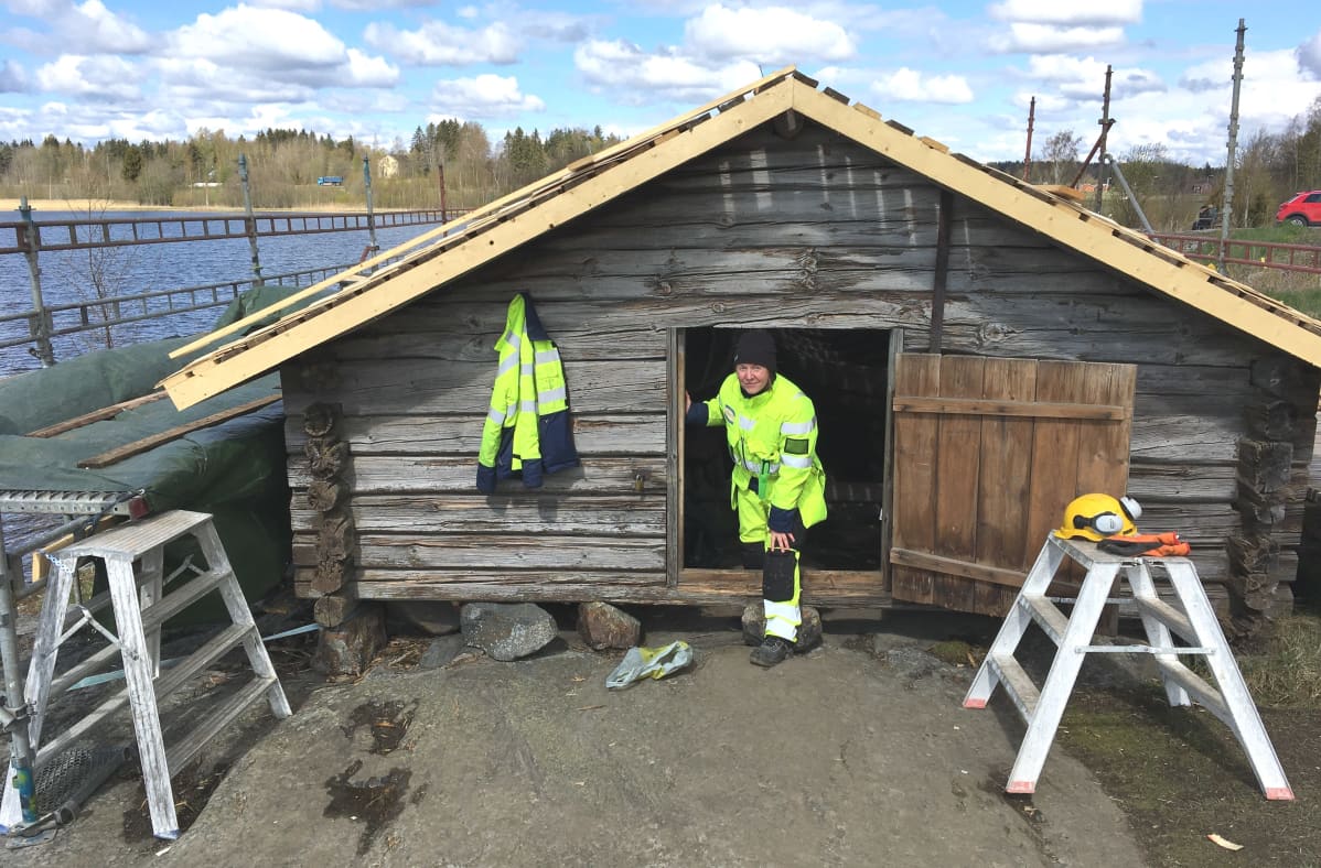 Nainen seisoo vanhan hirrestä rakennetun venevajan ovella.