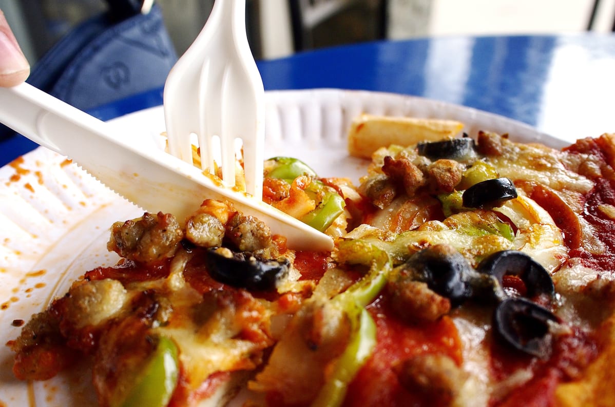 henkilö syö pizzaa kertakäyttöaterimilla