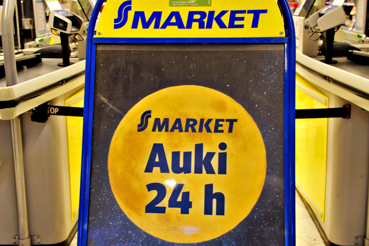 Helsingin Sokoksen alakerran S-marketin aukiolokylttejä. Mainoksessa on keltainen täysikuu, jossa lukee: "Auki 24h"