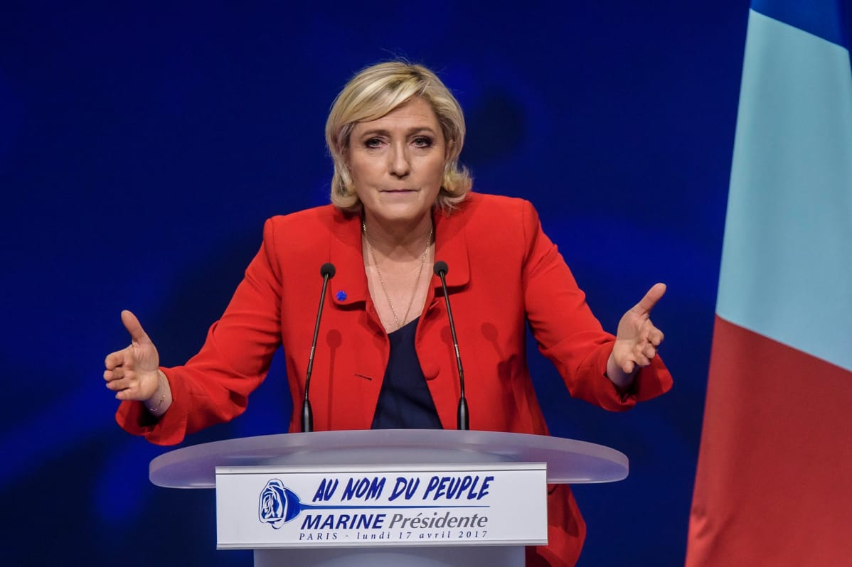 Marine Le Pen puhujakorokkeella punaisessa takissa