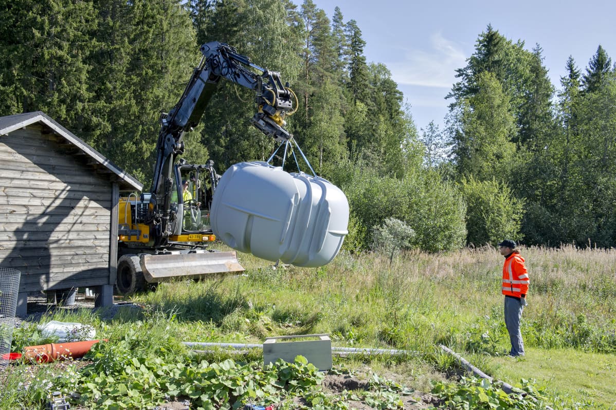 Tontille toimitettu jätevesisäiliö siirretään kaivurillla asennuskuoppaan.