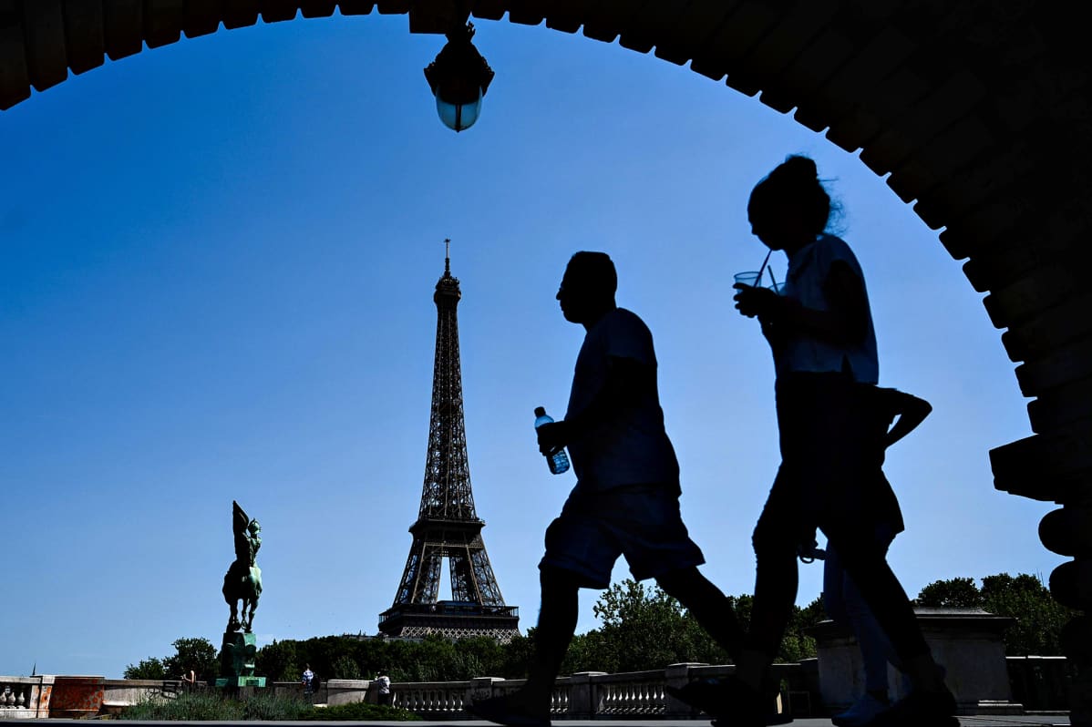 Siluettikuvassa mies pitää vesipulloa ja nainen juo pillillä muovilasista Eiffel-tornin lähistöllä Pariisissa.