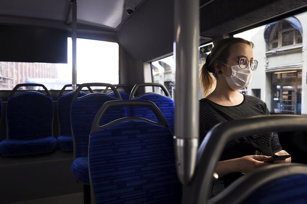 Hengityssuojainta käyttävä nainen matkustaa bussilla Helsingissä.