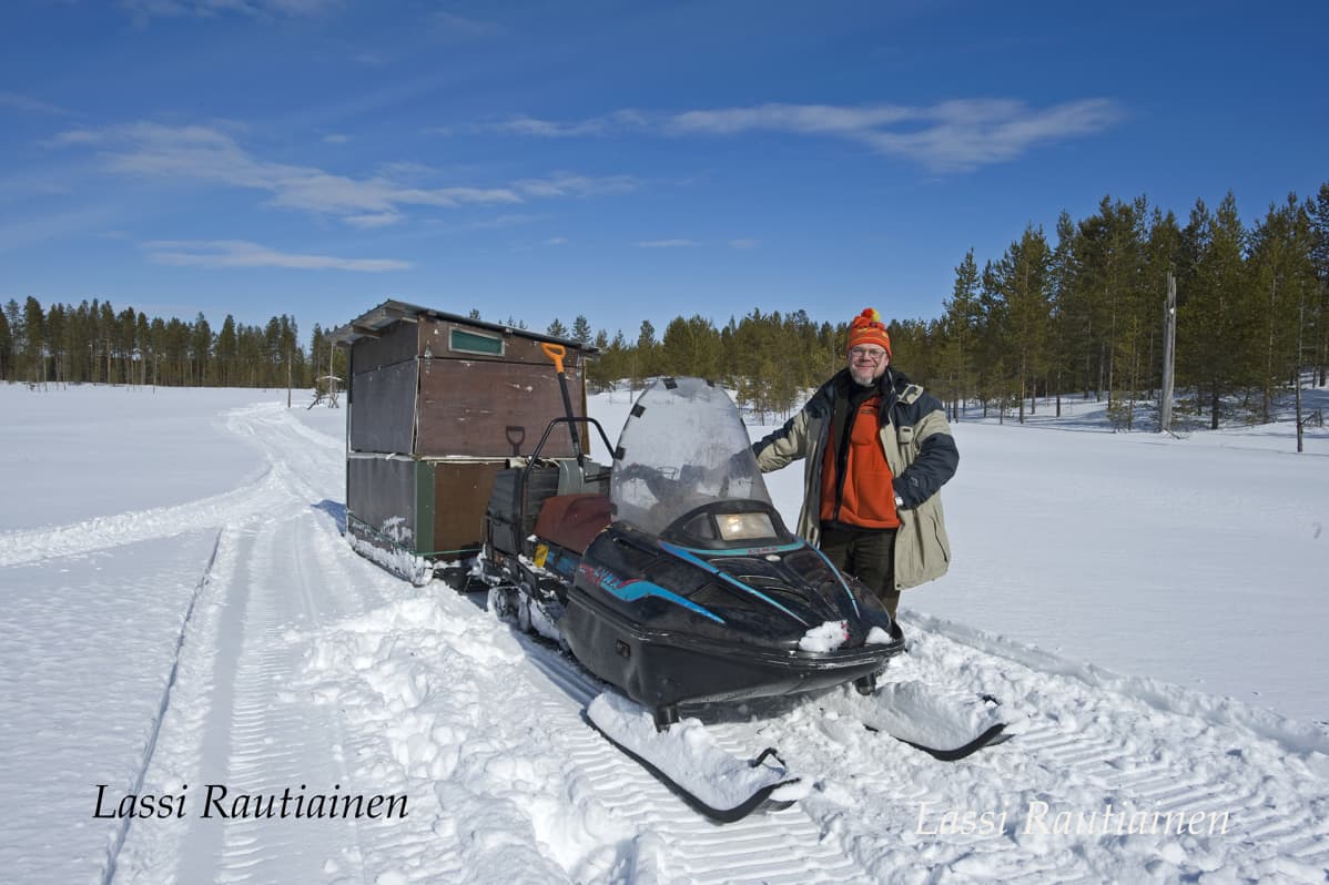 Mies seisoo moottorikelkan vieressä.