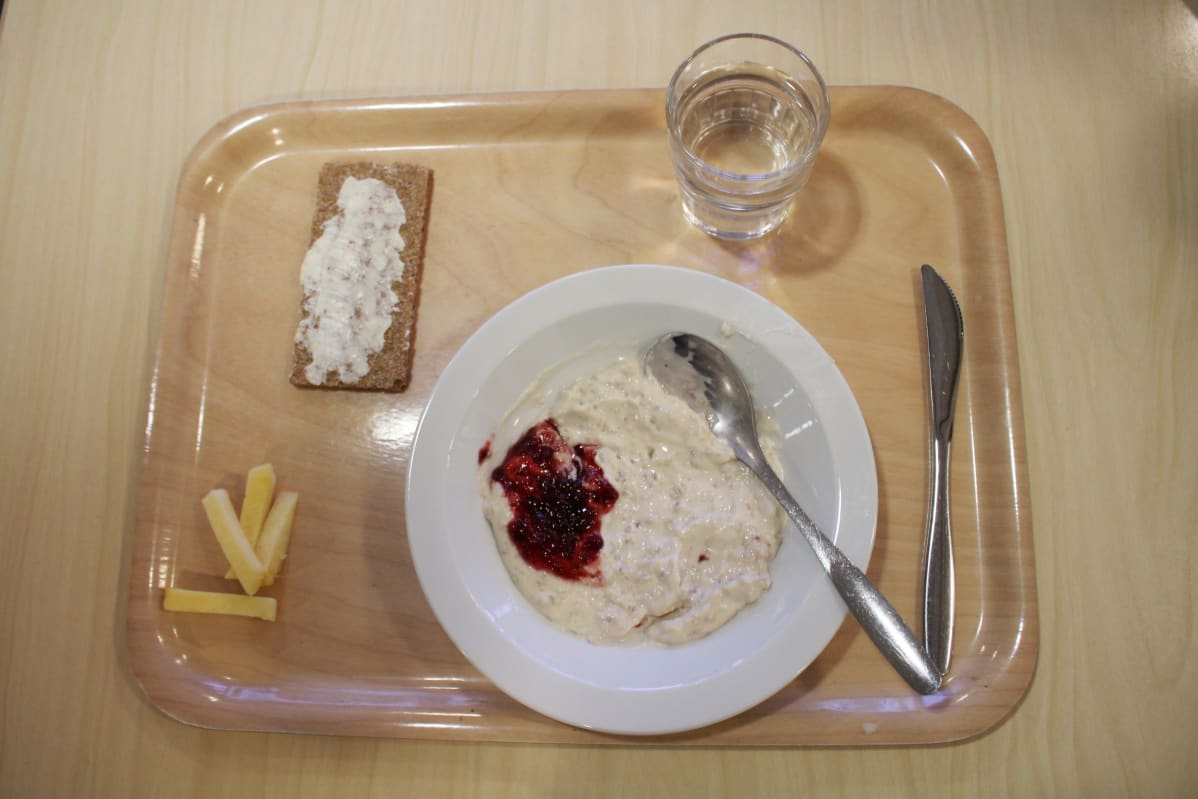 Tarjottimella kouluruokaa: ohrapuuroa, näkkäri ja lasi vettä.