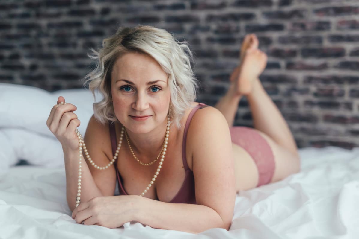 Elina Pynnönen poseeraa boudoir-kuvassa sängyllä vaaleanpunaisissa alusvaatteissa.