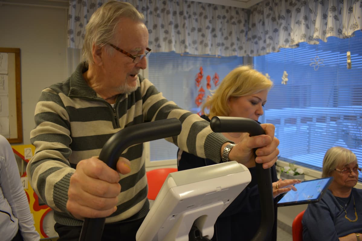 Reino Ilola antaa ohjeita, minne haluaa ajaa. Minna Laine näppäilee osoitteen kartalle. Sen jälkeen reitti avautuu televisioruudulle.