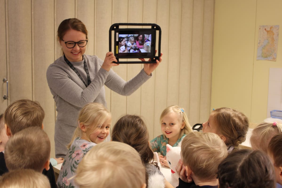 Kotkan varhaiskasvatuksen kehittämiskoordinaattori Tiina Kääpä näyttää lapsille näiden keksimää tarinaa tabletin näytöltä.