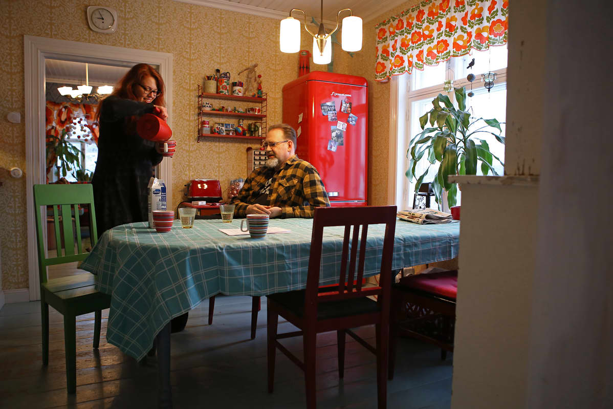 Mies istuu ruokapöydän ääressä ja nainen kaataa kahvia.