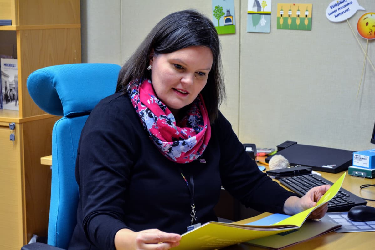 Heidi Hänninen työpöytänsä ääressä selailee esitettä.