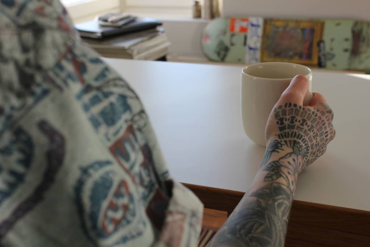Tatuoitu käsi ja kahvikuppi